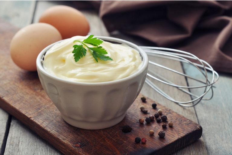 receita de maionese caseira: tigela com maionese decorada com cebolinha. Dois ovos e um fuê ao lado da tigela.