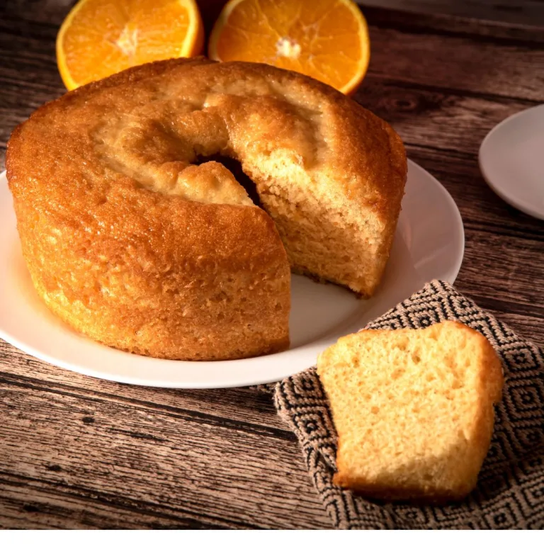 receita bolo de laranja: bolo com uma fatia cortada e uma laranja cortada ao meio do lado.