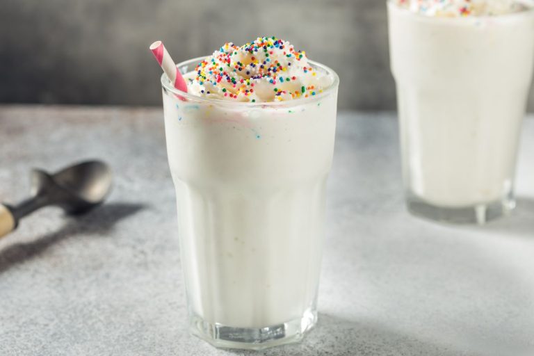 como fazer milk shake: como com milk shake de baunilha. Chantilly , confeitos coloridos e um canudo.