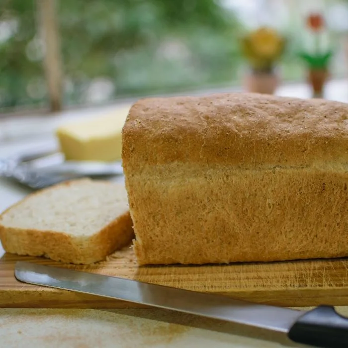 receita de pão caseiro fofinho: pão caseiro com um afatia cortada e uma faca ao lado.