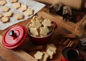 biscoito amanteigado em uma panelinha vermelha e uma assadeira com mais biscoitos ao lado.