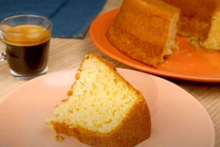 receita de bolo caseiro simples: bolo cortado uma fatia em um prato com xícara de café ao lado.