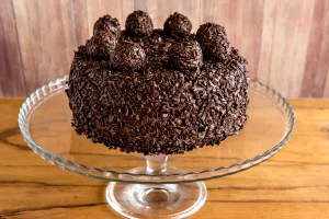 bolo de aniversário de brigadeiro em uma boleira de vidro transparente lindamente decorado com brigadeiros em cima.