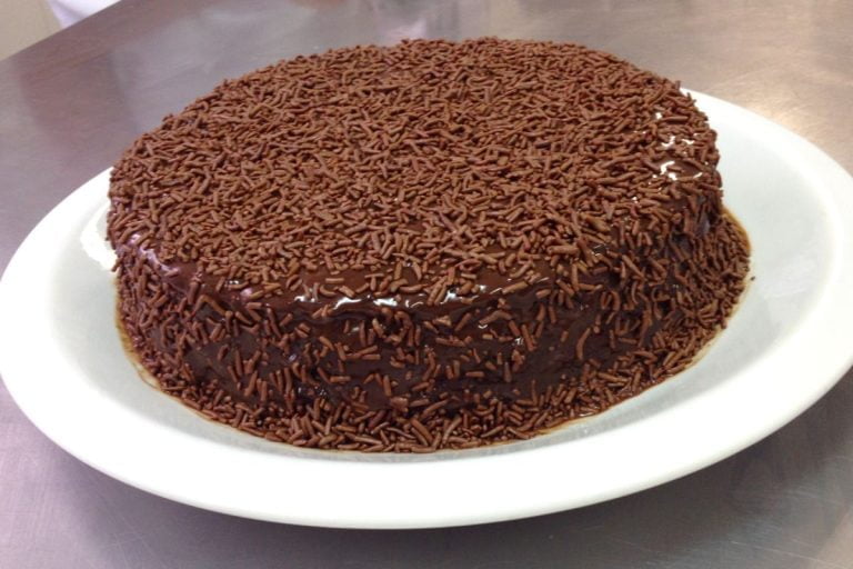 bolo de chocolate fofinho com cobertura de chocolate e granulado em um prato pronto para ser servido.