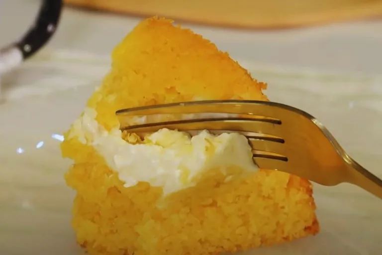 fatia de bolo de milho em lata com requeijão sendo servido com garfo dourado.