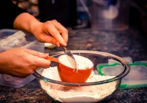 mulher colocando uma xícara de farinha em uma vasilha para fazer um bolo simples