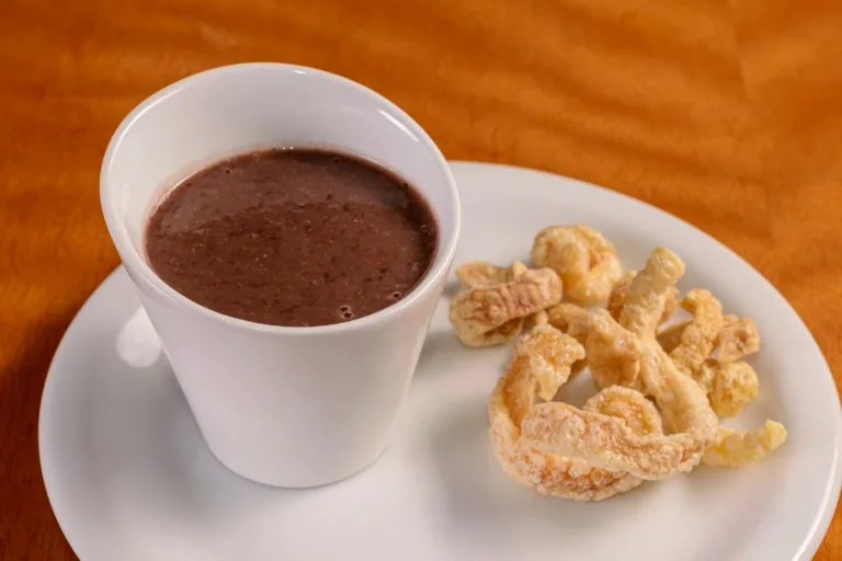 caldo de feijão preto em um copinho branco com torresmos ao lado.