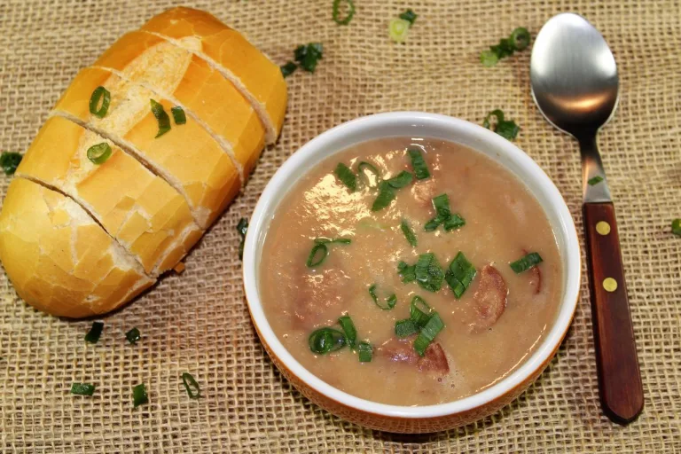 tigela com delicioso caldo de feijão com pão francês ao lado e uma colher.