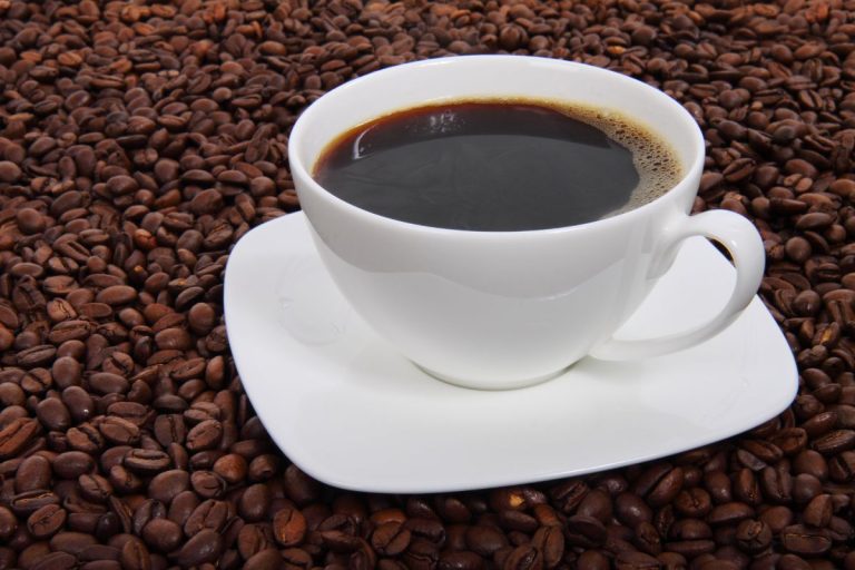 como fazer café: xícara branca com café em cima de vários grãos de café.