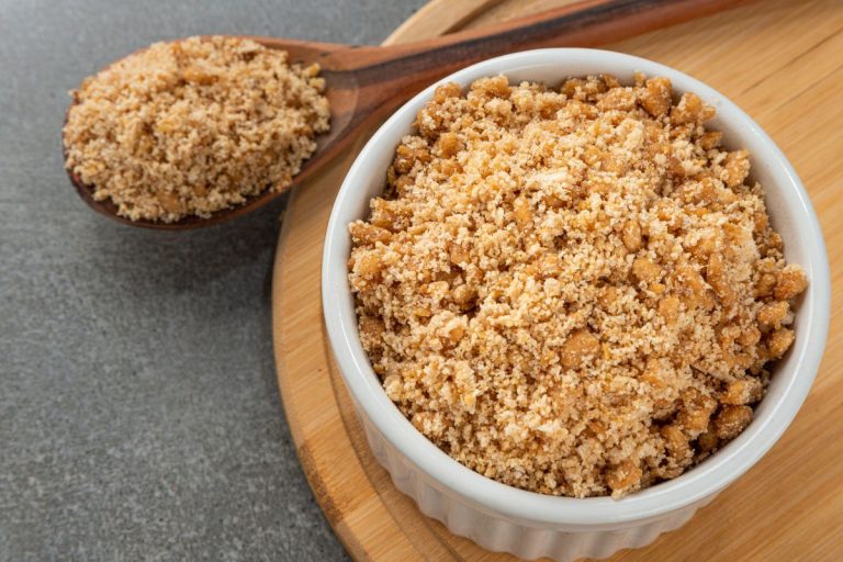 farofa para comer com peixe: farofa em uma tigela pequena branca com uma colher de pau ao lado.