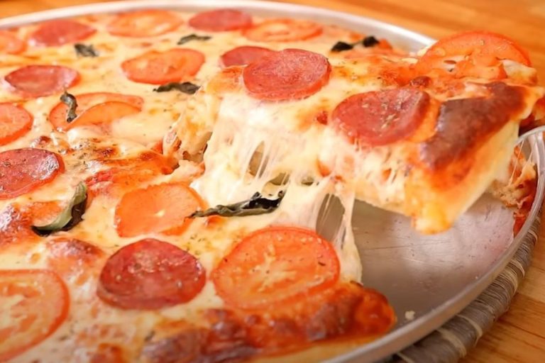 pizza 2020 recheada de tomate e calabresa sendo fatiada.