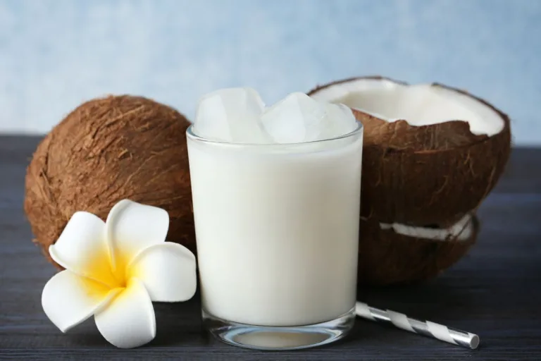 batida de coco em um copo com cocos e uma flor branca ao lado