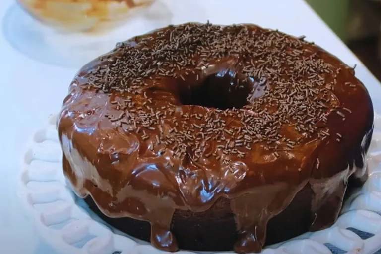 delicioso bolo de cacau com cobertura cremosa e chocolate e granulado em um prato branco pronto para ser servido.