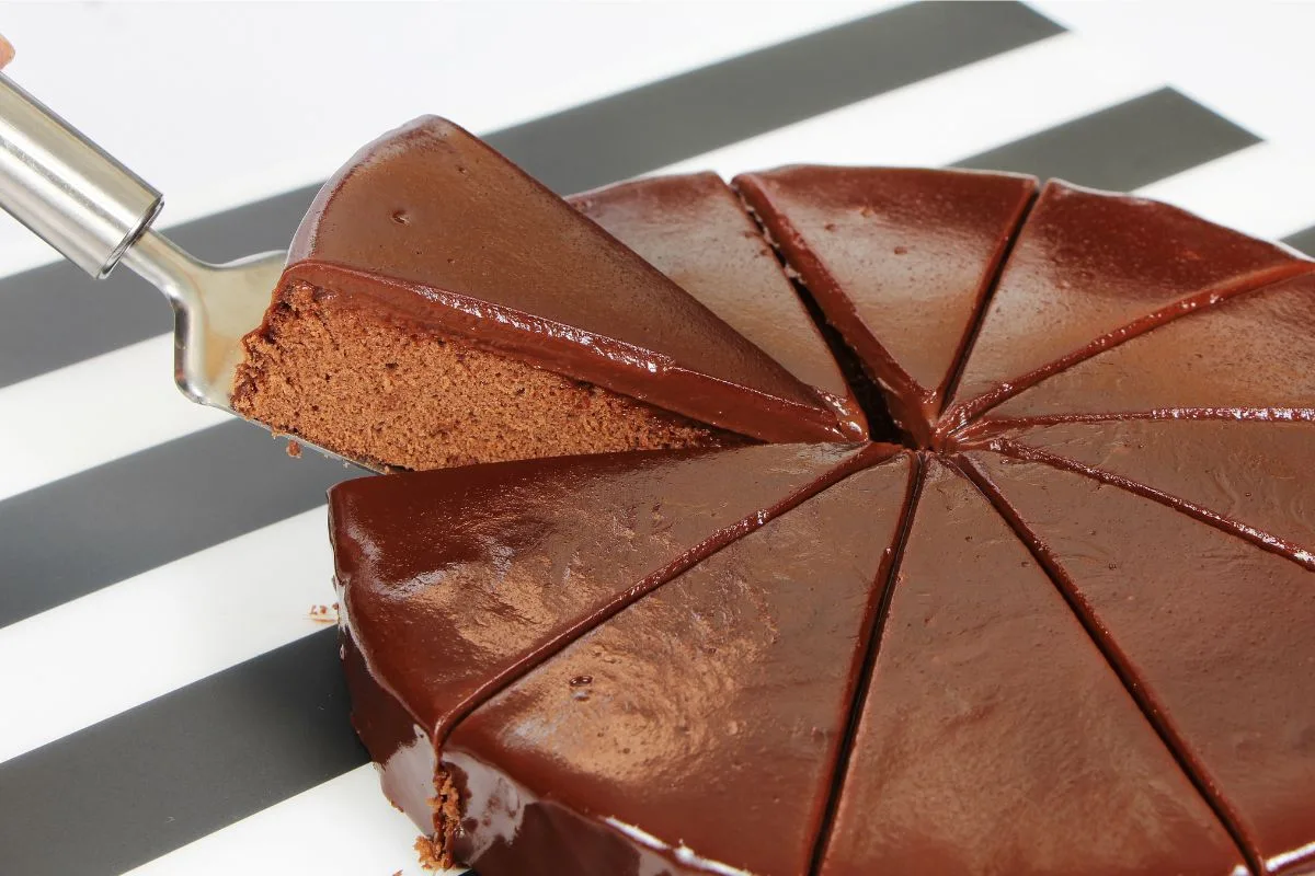 bolo redondo de chocolate sendo fatiado para servir.