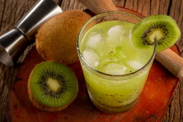 Origem/História da Receita: caipirinha de kiwi em um copo decorado. Com kiwis ao lado.