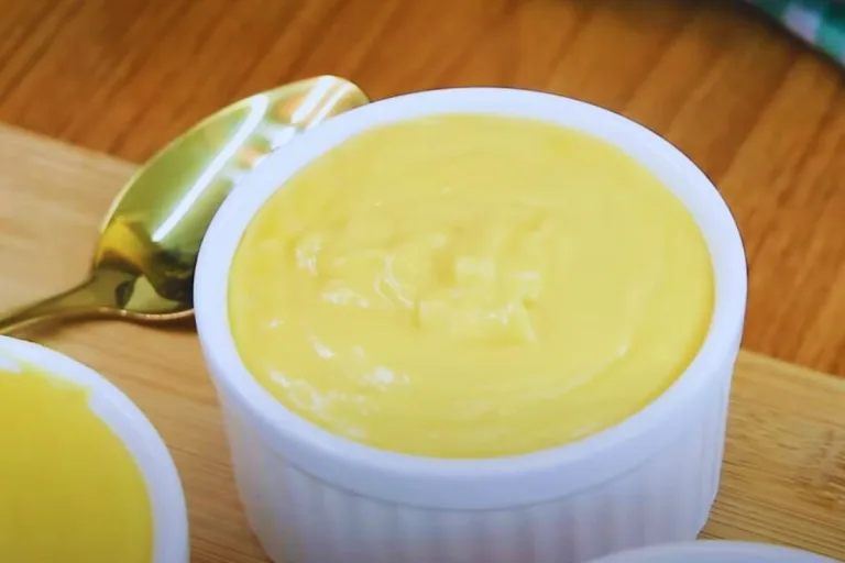 receita de curau de milho de liquidificador: curau cremoso em um potinho branco e uma colher dourada ao lado.