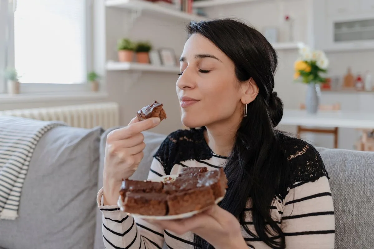 mulher comendo um pedaço de bolo com pratinho nas mãos com outros pedaços de bolo de chocolate.