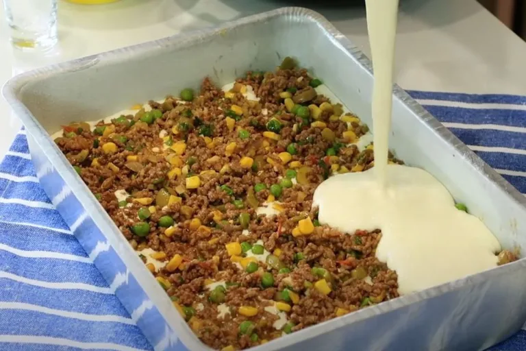 torta simples sendo preparada em uma assadeira com recheio de carne moída.